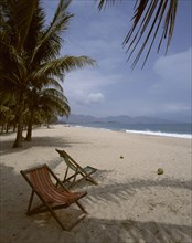 VIETNAM, South, Nha Trang, "Beach,golden sand,two empty deckchairs,palm trees,distant hills "