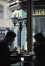 FRANCE, Normandy , Rouen, A back lit couple sat eating and drinking in a Cafe interior.