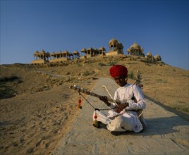 INDIA, Rajasthan, Jaisalmer, Musician wearing a red turban sitting cross-legged on the ground with