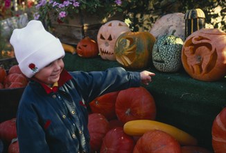 ENGLAND, West Sussex, Slindon, Child pointing at pumpkin display.