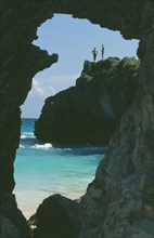 BERMUDA, Jobsons Cove, Two people on cliff across beach seen through cave