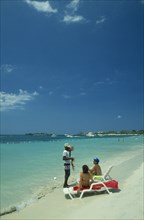 WEST INDIES, Jamaica, Negril, Man selling lobster to tourists on beach sitting on sun loungers by