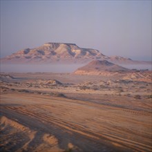 UAE, Abu Dhabi, "Nr Ruwais, Desert and hills with vehicle tracks on flat area in foreground seen on