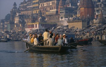 INDIA, Uttar Pradesh, Varanasi, Tourists in boat being rowed passed the ghats on the River Ganges.
