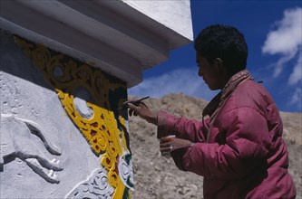 INDIA, Ladakh, Leh Valley, Young monk repainting the temple exterior.