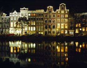 HOLLAND, North, Amsterdam, Canalside houses and lights reflected in water at night.