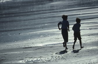 ENGLAND, East Sussex, Hastings, Two boys running along the wet sand of the beach
