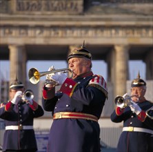 GERMANY, Berlin, Brass bandsmen in traditional uniform playing trumpet with the Brandenburg Gate