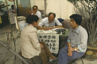 CHINA, Shaanxi, Xian, Professional letter writer with customers sitting at a desk outside the post