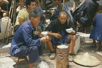 CHINA, Markets, Eating, Two elderly men cooking meal at roadside stall.