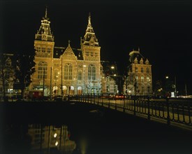 HOLLAND, North, Amsterdam, Rijksmuseum illuminated at night beyond a bridge over a canal reflected