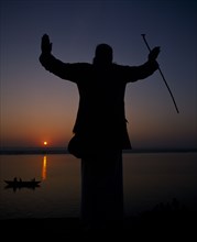INDIA, Uttar Pradesh, Varanasi, Silhouette at sunset of a Holy Man on the banks of the River Ganges