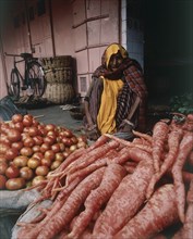 INDIA, Rajasthan, Jaipur, Female vegetable seller with red root vegetables and tomatoes