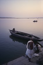 INDIA, Uttar Pradesh, Varanasi, Man gutting fish on the rivers edge with nearby boat