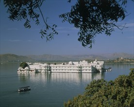 INDIA, Rajasthan, Udaipur, The Lake Palace in the middle of the lake with a covered boat making its
