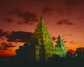 INDIA, Tamil Nadu, Mahabalipuram, Shore Temple.  Tower floodlit at dusk with dramatic orange sky