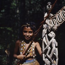 INDONESIA, Irian Jaya, Sorong, Young girl beside wooden carvings