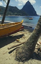 WEST INDIES, St Lucia, Soufriere, Fishing boat by coconut palm tree on beach with the Pitons in the