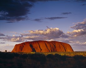 AUSTRALIA, Northern Territory, Uluru, Ayers Rock.  Giant red rock formation at dusk overshadowed by