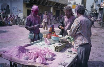 INDIA, Rajasthan, Pushkar, Holi Festival paint stall with people and street covered in layer of