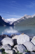 CANADA, Alberta, Lake Louise, View over boulders and clear blue water toward snow covered rocky