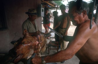 CUBA, Palma Soriano, Man standing at spit carving a whole roasted pig with a large knife