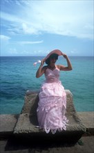 CUBA, Varadero, Girl sitting on sea wall wearing a pink party dress for her 15th birthday