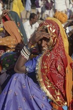 INDIA, Rajasthan, Pushkar, Seated smiling Rajasthani woman in colourful sari looking over her