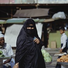UAE, Dubai, Arab woman in black wearing yashmak at local market