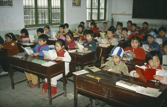 CHINA, Hunan Province, Huaihua, Primary school children reading at desks in classroom.
