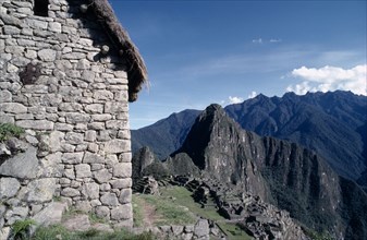 PERU, Cusco, Machu Picchu, View of the side of a stone built thatched house with ruins beyond