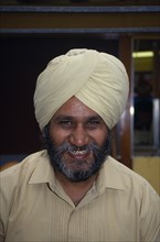 ENGLAND, London, Head and shoulders portrait of a Sikh man smiling wearing a beige turban