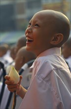 THAILAND, North, Chiang Mai, Laughing novice monk dressed in white holding a lotus flower during a