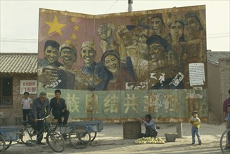 CHINA, Ningxia, Guyuan , Old Communist poster on hoarding at road junction with woman selling fruit