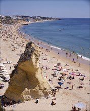 PORTUGAL, Algarve, Albufeira, View along the beach from above with a large rock and sunbathers.