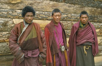 CHINA, Tibet, Bomi, Three Tibetan monks standing against wooden exterior wall of building.