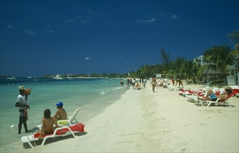 WEST INDIES, Jamaica, Negril, Man selling lobster to tourists on beach sitting on sun loungers by