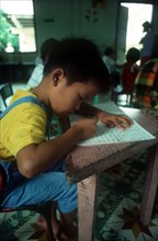 VIETNAM, Ho Chi Minh City, Child writing at a desk in an Agent Orange Orphanage.