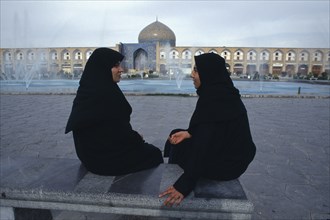 IRAN,  , Esfahan, Emam Khomeini Square Two women talking Sheikh Lot Fallah mosque in background