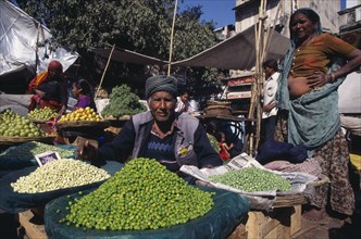 INDIA, Gujarat, Ahmedabad, Vegetable market vendor selling fresh beans and peas.