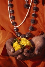 INDIA, Maharashtra, Nasik, Cropped shot of figure in orange robes and wearing prayer beads.  Close