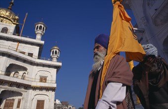 INDIA, Punjab, Amritsar, Golden Temple with a pilgrim flag bearer carrying the Sikh orange flag or