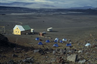 ICELAND, Central, Several blue tents camping in a lava field beside a small building