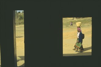 KENYA, Voi, Women carrying baskets framed by window of building in deep shadow.