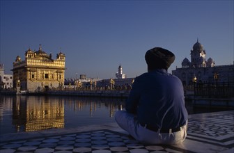 INDIA, Punjab, Amritsar, Golden Temple with pilgrim sat beside sacred pool in the foreground.