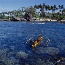 INDONESIA, Irian Jaya, Sorong, Children in outrigger canoe with beach behind