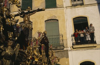 SPAIN, Andalucia, Seville, Semana Santa Easter procession with a family watching from balcony
