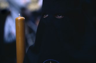 SPAIN, Andalucia, Seville, Semana Santa Easter procession. Penitent in black robe with eyes visable
