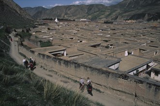 CHINA, Gansu, Xiahe , View over the rooftops of the Labrang Monastery with people walking a path