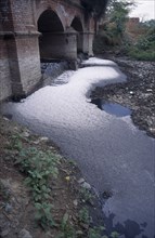 INDIA, Uttar Pradesh, Agra , Polluted river.  Scum and foam covered water flowing through arches in
